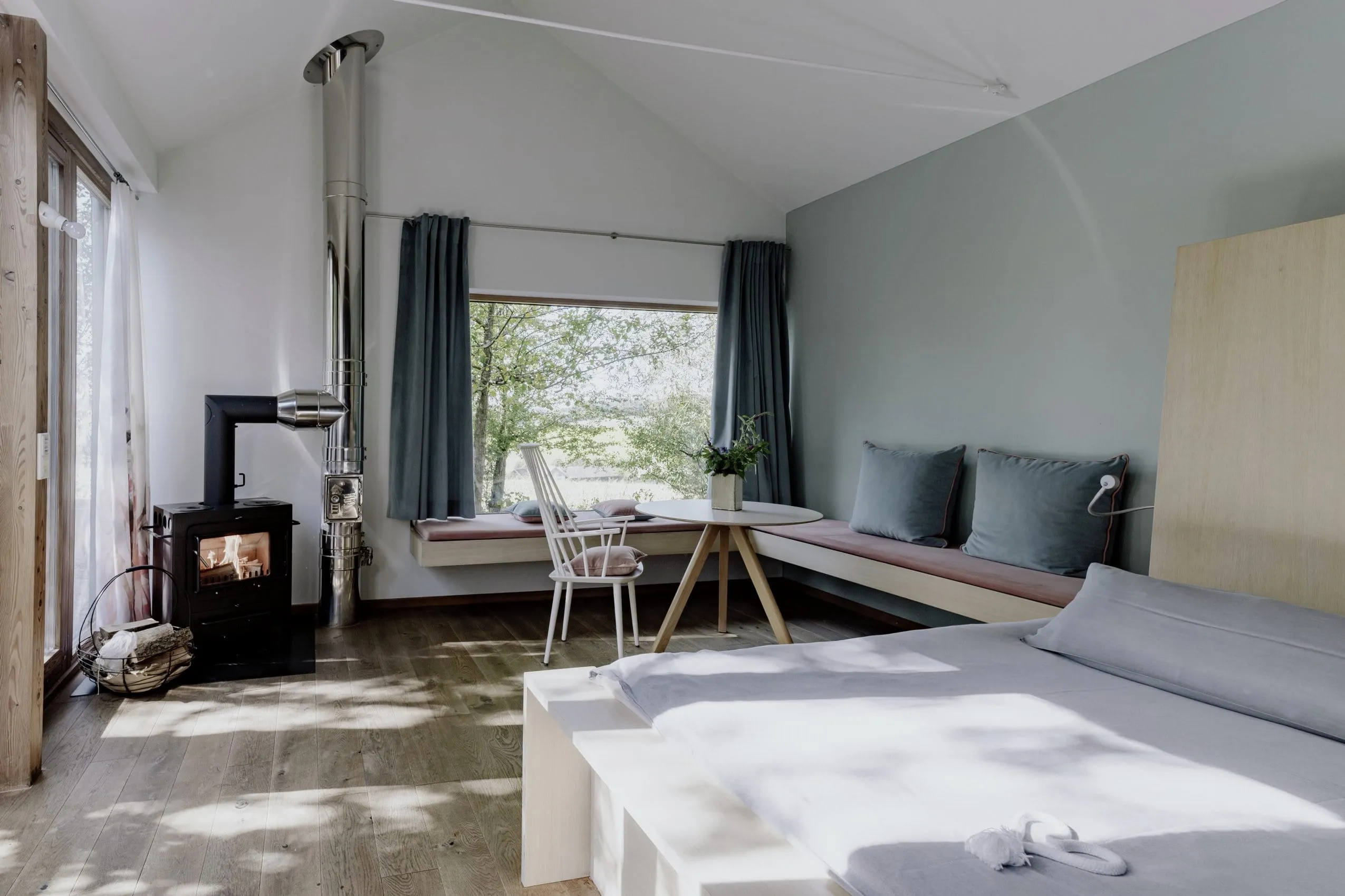 Doppelbett, gem&uuml;tliche Sitzecke mit mintfarbener Wand, Kissen und Vorh&auml;ngen, wei&szlig;em Stuhl und kleinem Kamin auf dem Hofgut Hafnerleiten