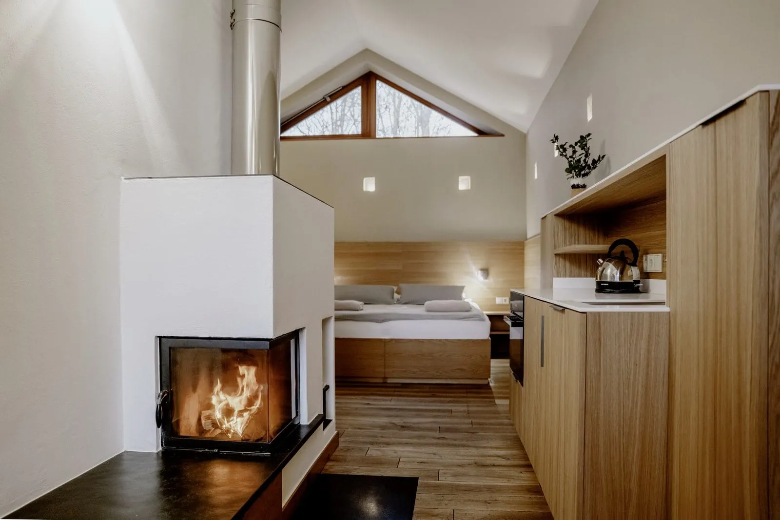 Kleines gem&uuml;tliches Zimmer mit warmen Holzt&ouml;nen am Bett, der Wand und der kleinen K&uuml;chenzeile. Ein kleiner Kamin sorgt f&uuml;r zus&auml;tzliche Gem&uuml;tlichkeit.