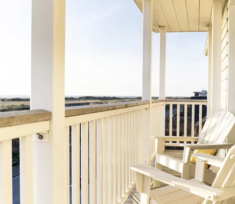 Balkon des Beach Motel St. Peter-Ording mit weißen Holzstühlen und weitem Blick auf die umliegende Landschaft bei blauem Himmel