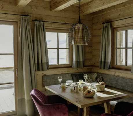 Essbereich in einem der Hygna Chalets mit Sitzecke, zwei bordeauxroten Polsterstühlen und gedecktem Frühstückstisch