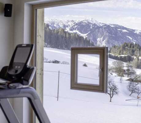 Blick vom Fitnessraum durch großes Panoramafenster nach draußen in die Schneelandschaft der Hygna Chalets