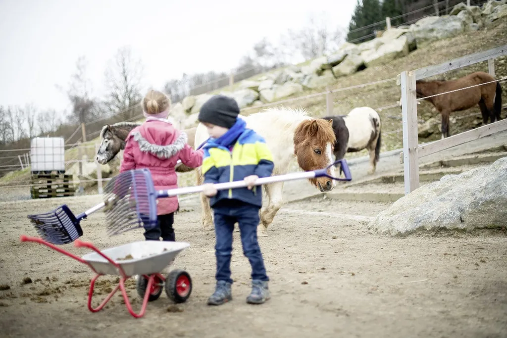 M&auml;dchen und Junge mit Mistgabel auf der Pferdeweide des Hotel & Resort Landhaus zur Ohe