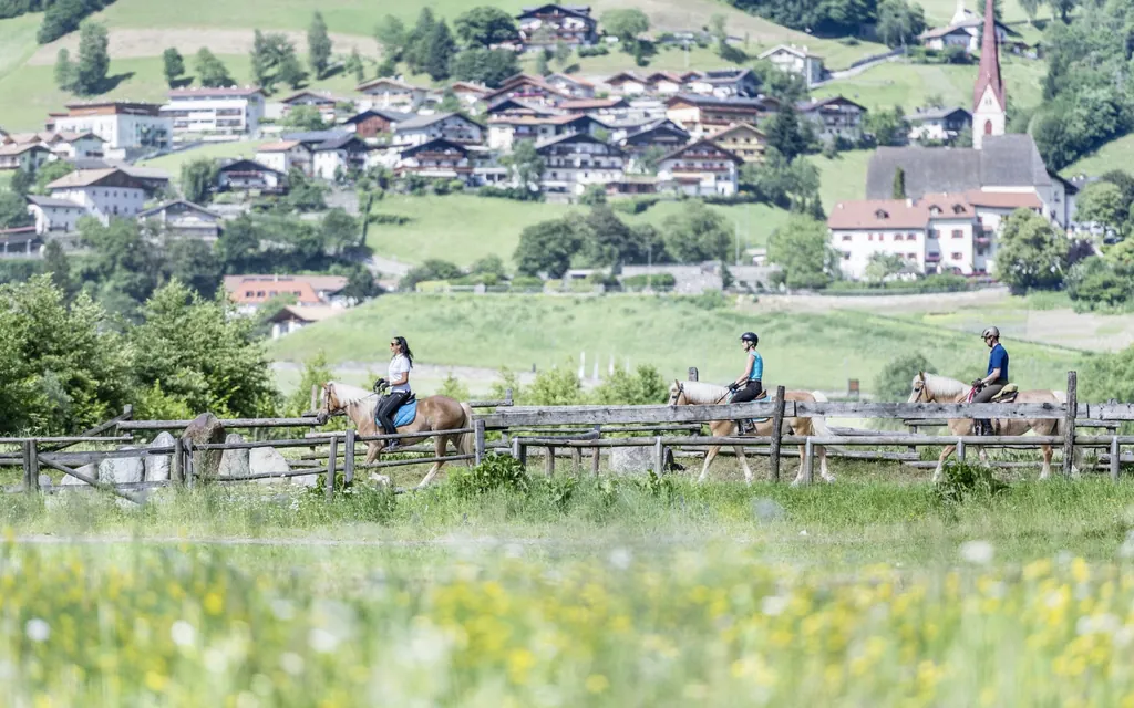 Drei Reiter bei einem Ausritt durch die Natur in der N&auml;he des Stroblhof - Active Family Spa Resort, Dorf im Hintergrund