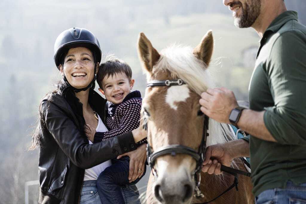 Eine lächelnde Familie mit kleinem Jungen und Pferd, draußen in ländlicher Umgebung des Stroblhof - Active Family Spa Resort