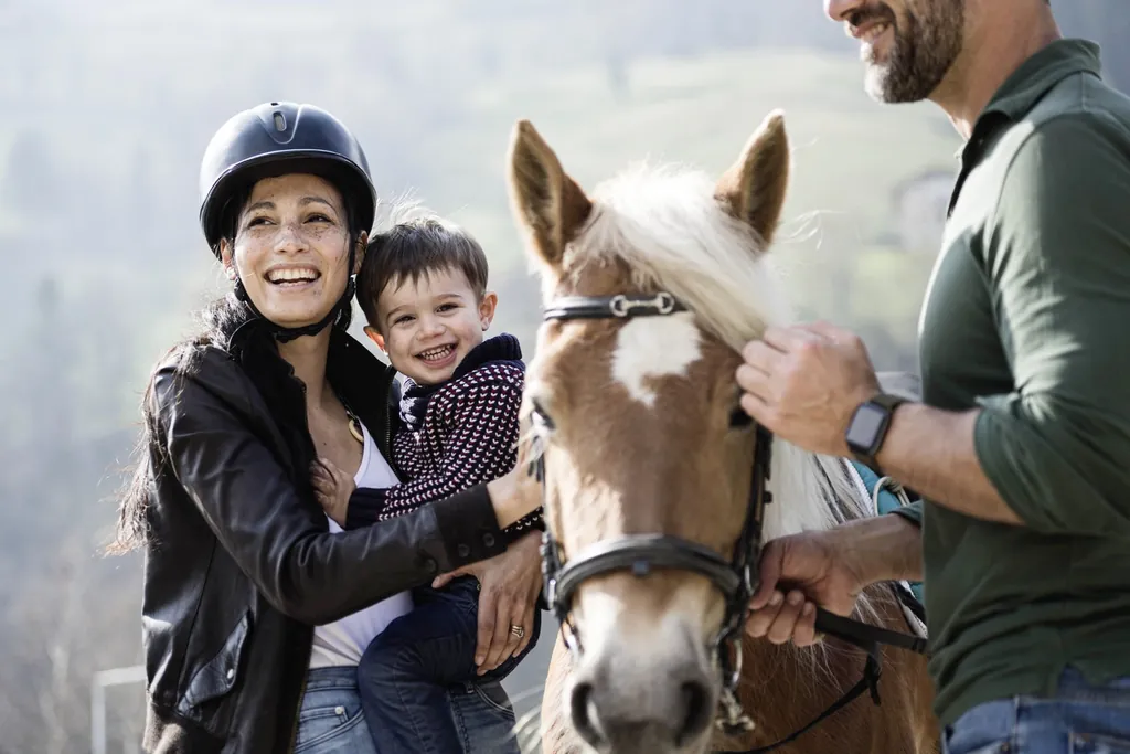 Eine l&auml;chelnde Familie mit kleinem Jungen und Pferd, drau&szlig;en in l&auml;ndlicher Umgebung des Stroblhof - Active Family Spa Resort