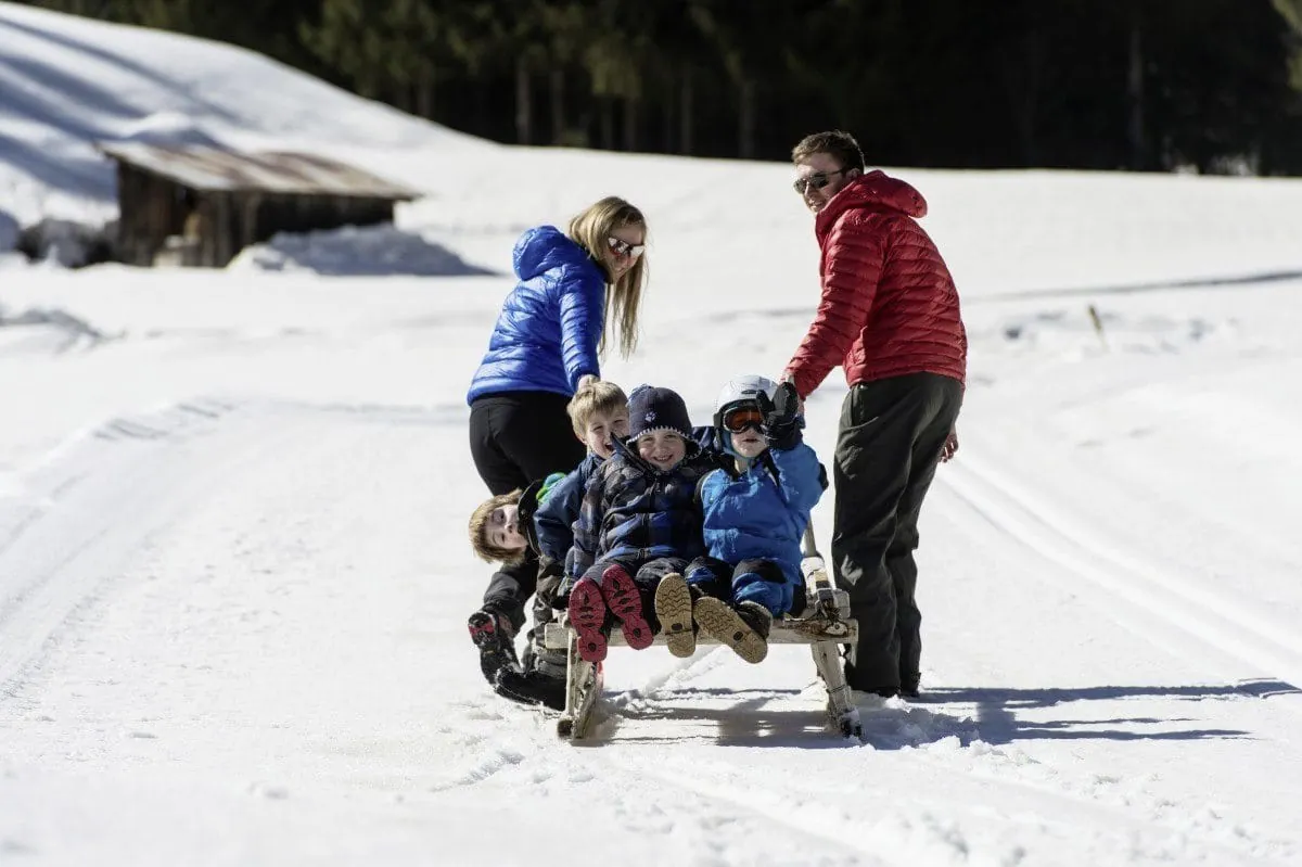 Mann und Frau in Daunenjacken ziehen im Hotel Alpin einen Schlitten mit vier KIndern in Kinderhotel in Suedtirol