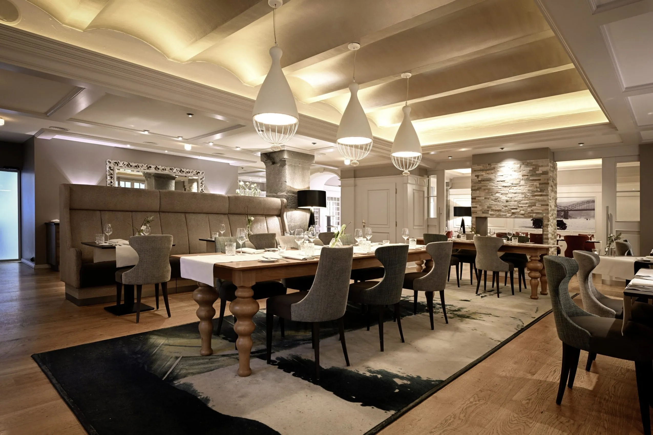 Restaurant im Moselschl&ouml;sschen mit langem alten Holztisch und wei&szlig;en Designer-H&auml;ngeleuchten