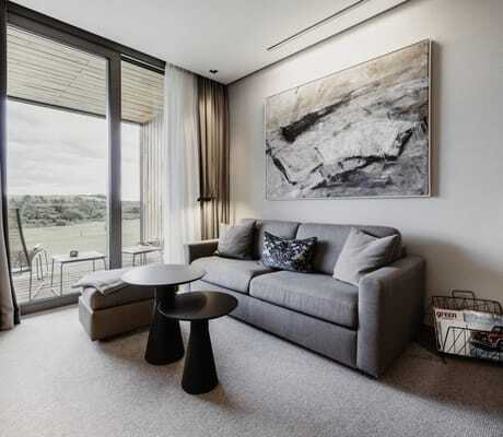 Graues Sofa in einem Zimmer des Öschberghofs mit runden schwarzen Beistelltischen und abstraktem Bild an der Wand