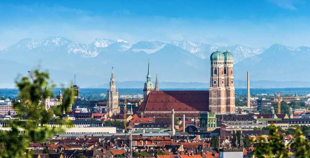 Skyline von München mit den berühmten Türmen der Frauenkirche. In der Ferne sieht man die Alpen.