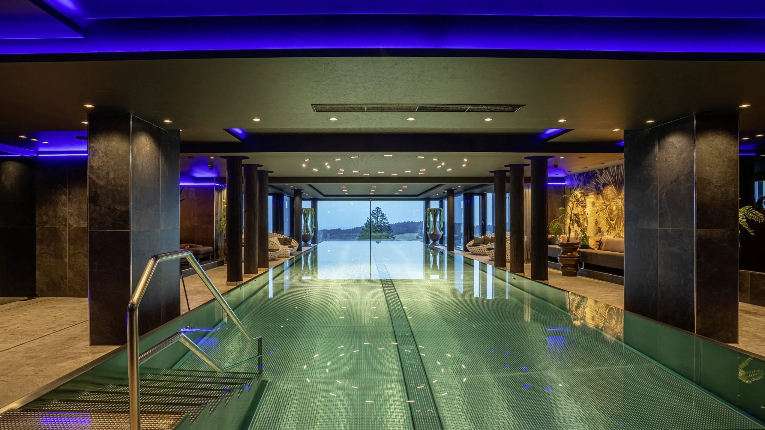 Indoor-/Outdoor-Infinitypool mit blauen Lichtleisten an der Decke und Blick auf einen Baumwipfel