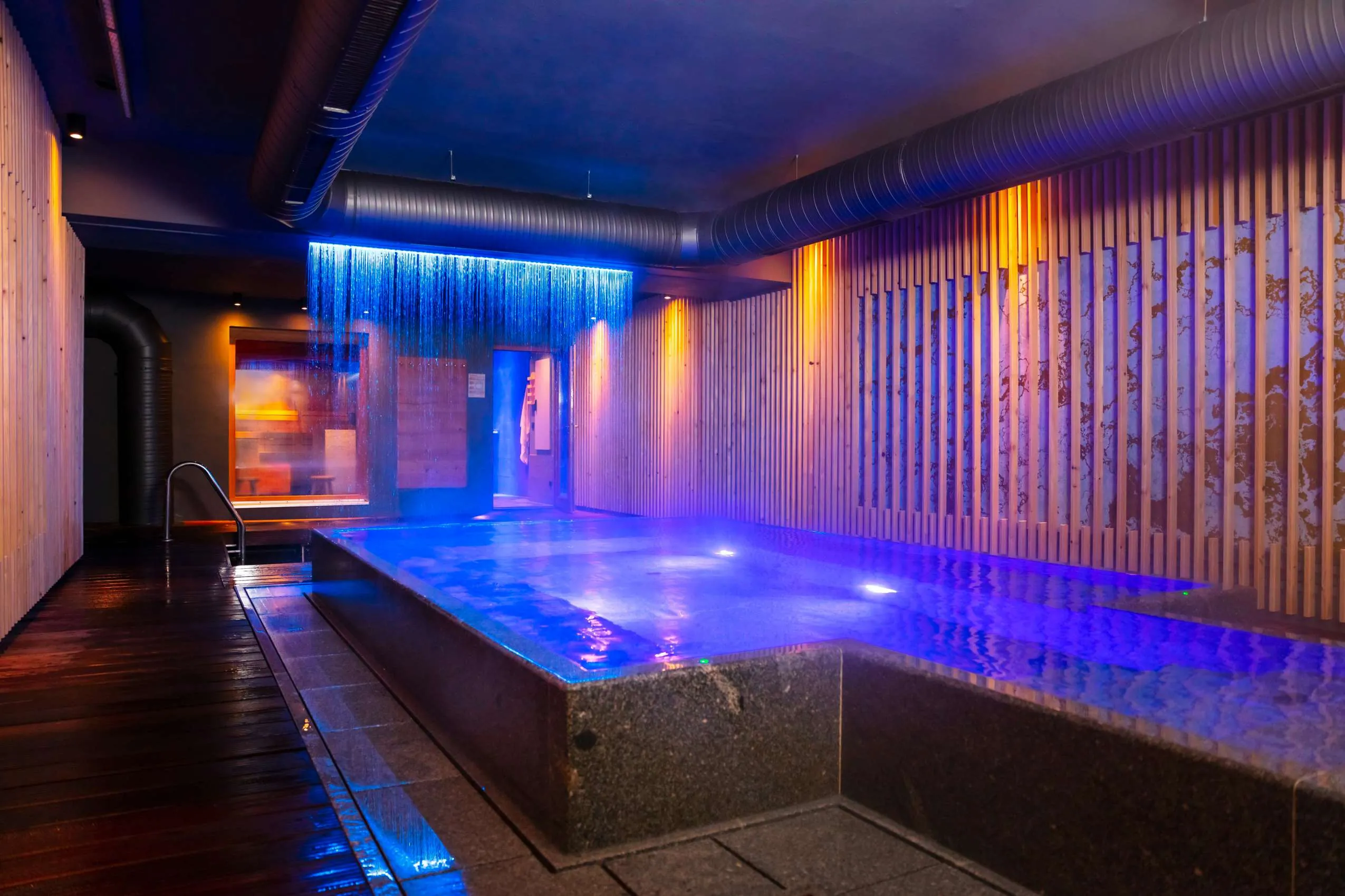 Innenpool mit stimmungsvollen blauen und orangen Lichtern und Regendusche