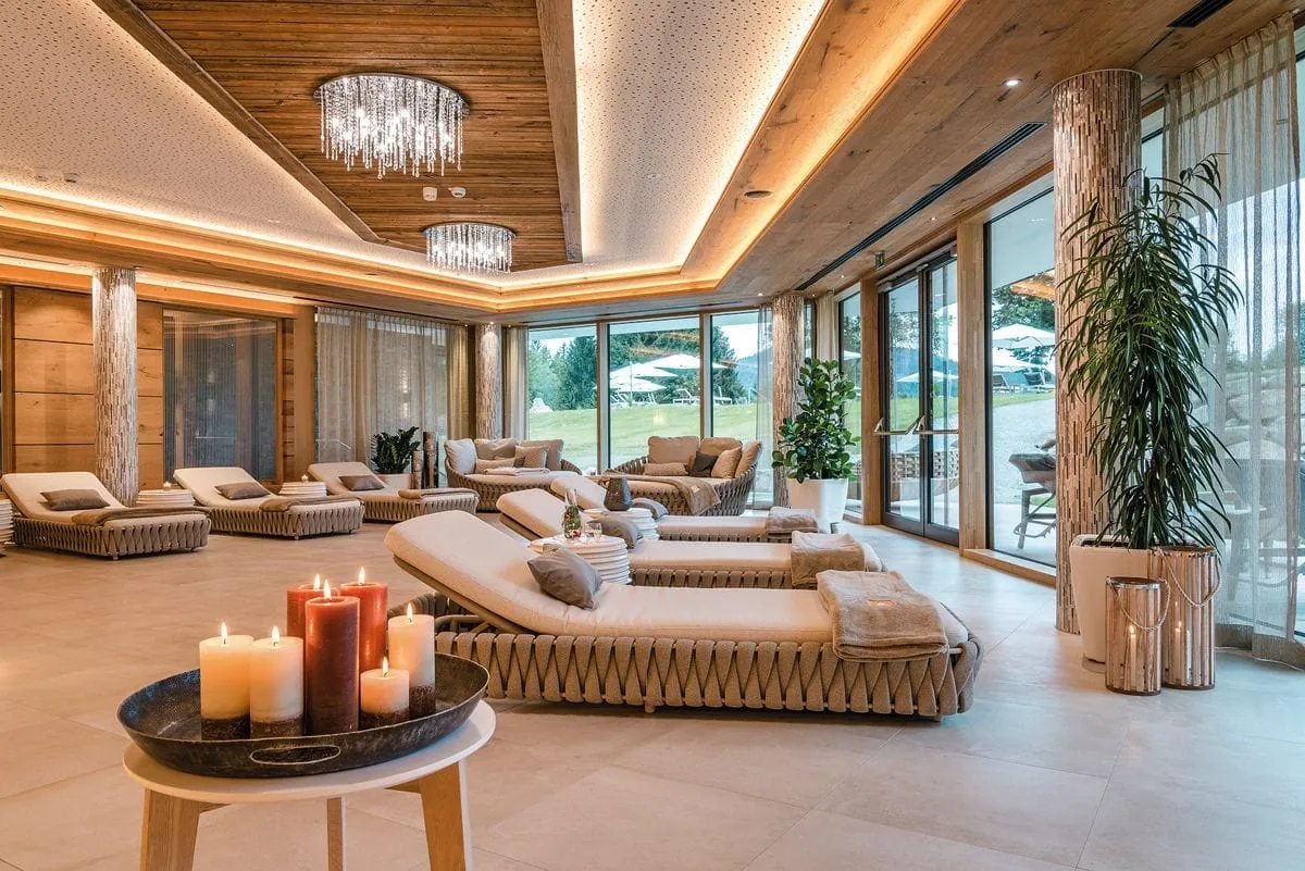 Luxuri&ouml;s, gem&uuml;tlicher Ruheraum des Mooshof mit warmen Beige- und Holzt&ouml;nen, bequemen Liegen, modernen Kristallleuchtern und einer gro&szlig;en Fensterfront.