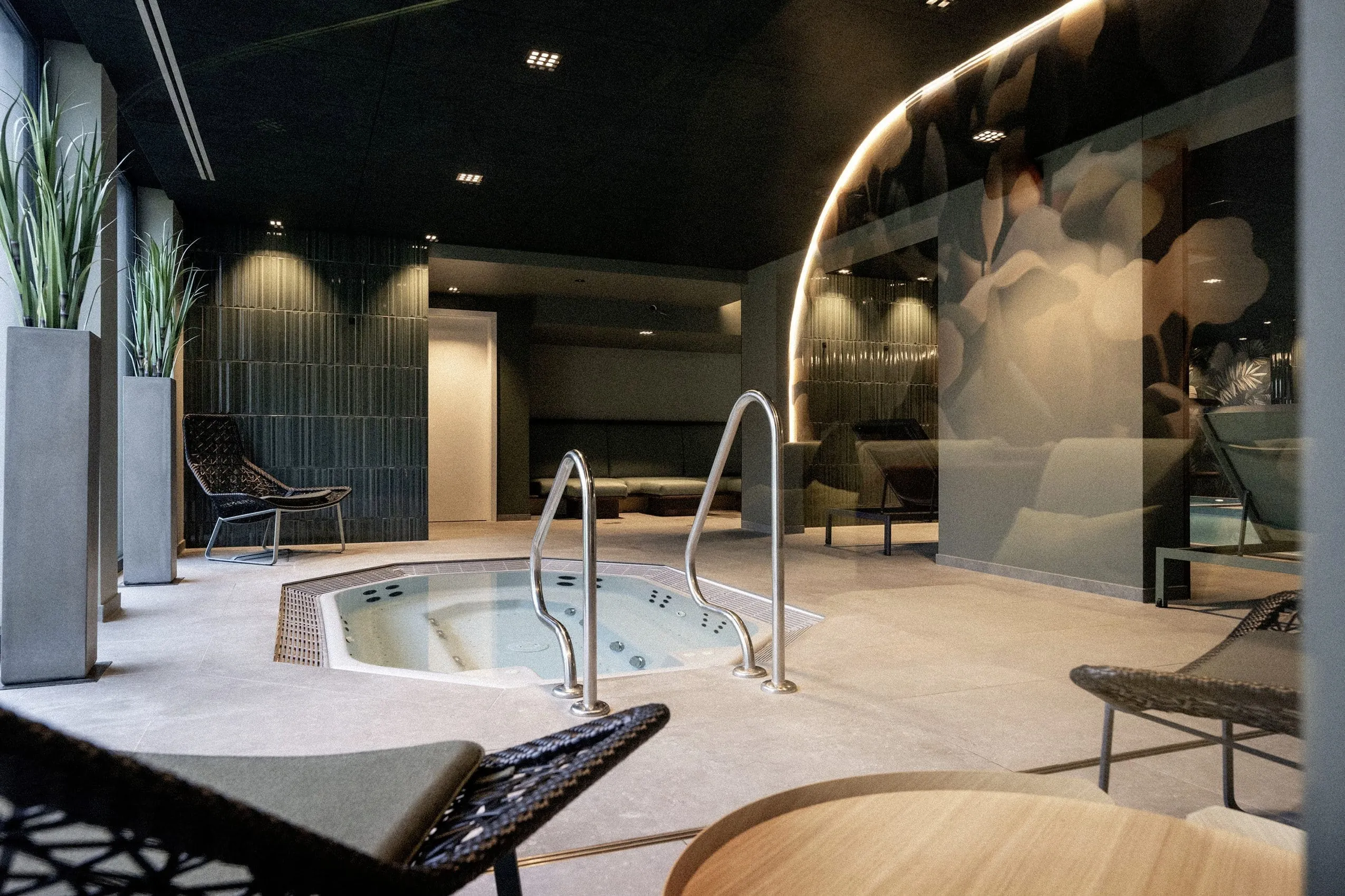 Wellnessbereich des Wellnesshotel Wittelsbach mit in den Boden eingelassenem Whirlpool, schwarzen Sesseln und sanfter Beleuchtung