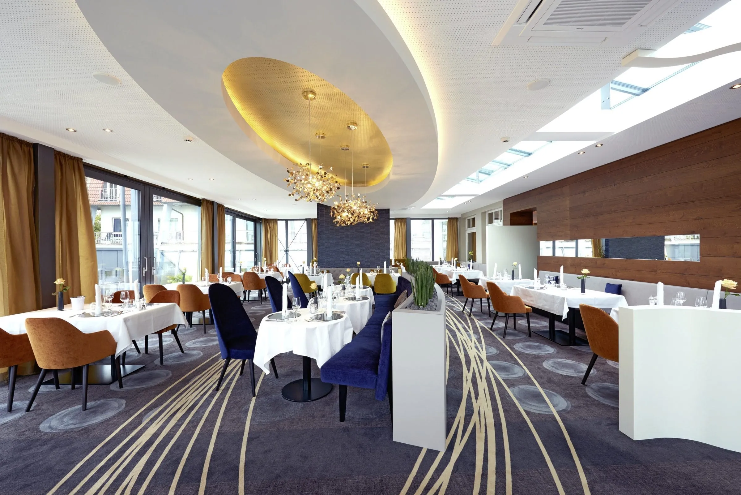 Restaurant des Hotel Heinz mit schick eingedeckten Tischen und Sessel in Kupfer- und Blauakzenten.