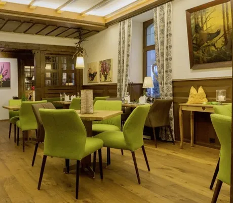 Stube im Waldhotel am Notschreipass mit grünen Polsterstühlen und pinkem Hirschbild