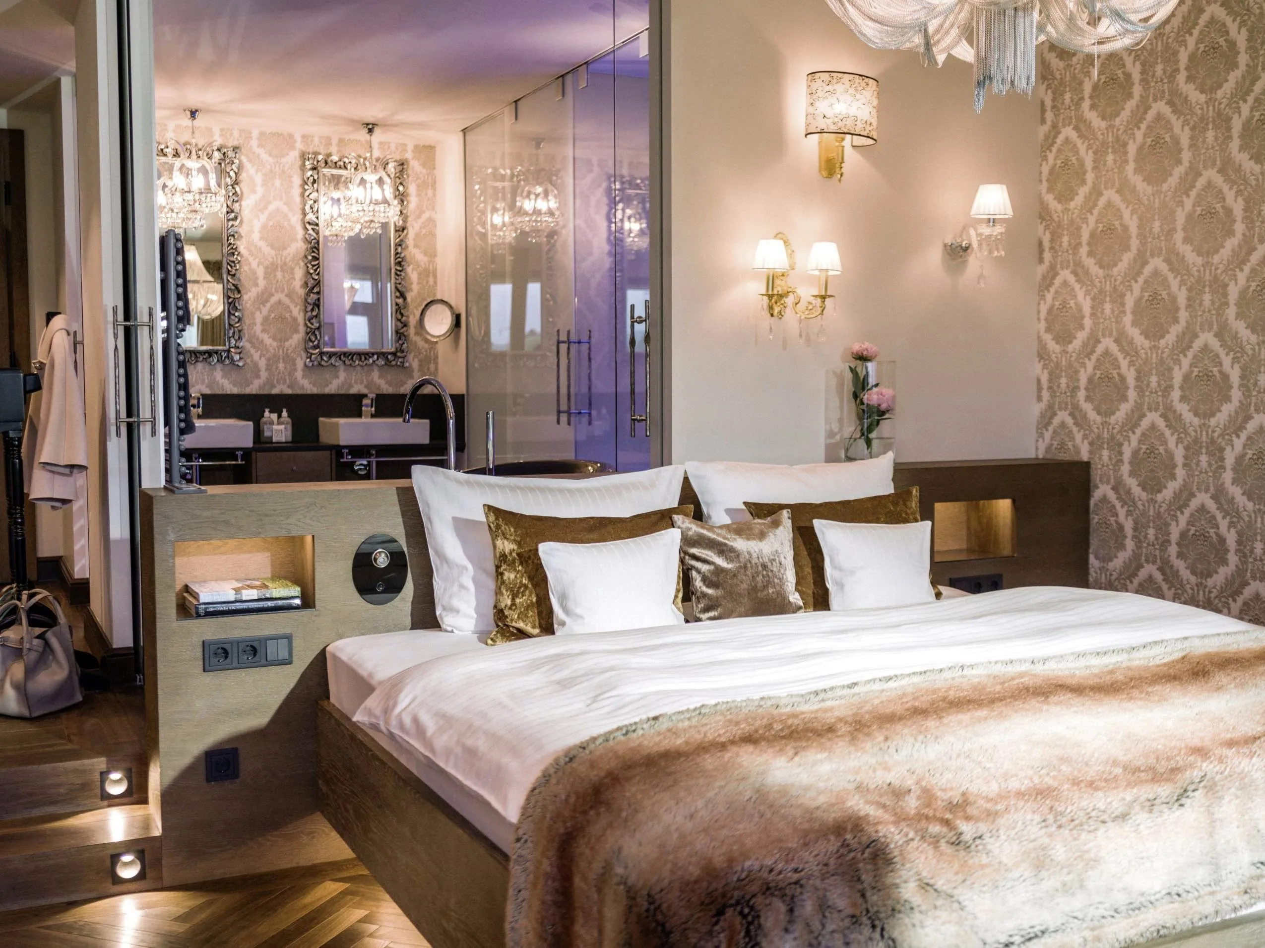 Luxuri&ouml;ses Schlafzimmer mit goldener Tapete, gro&szlig;em Bett mit goldenen Zierkissen und edlen Kronleuchtern.