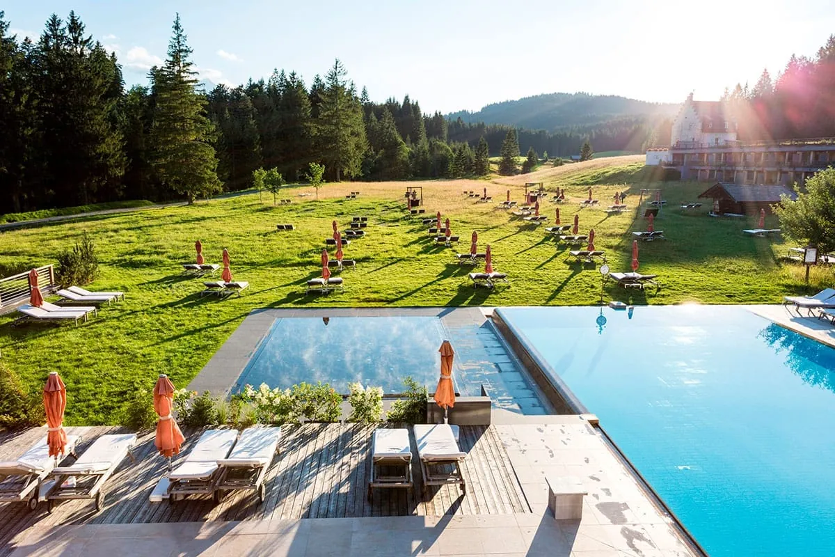 Au&szlig;enpool mit zahlreichen Sonnenliegen und Sonnenschirmen auf der Terrasse sowie auf der angrenzenden Liegewiese