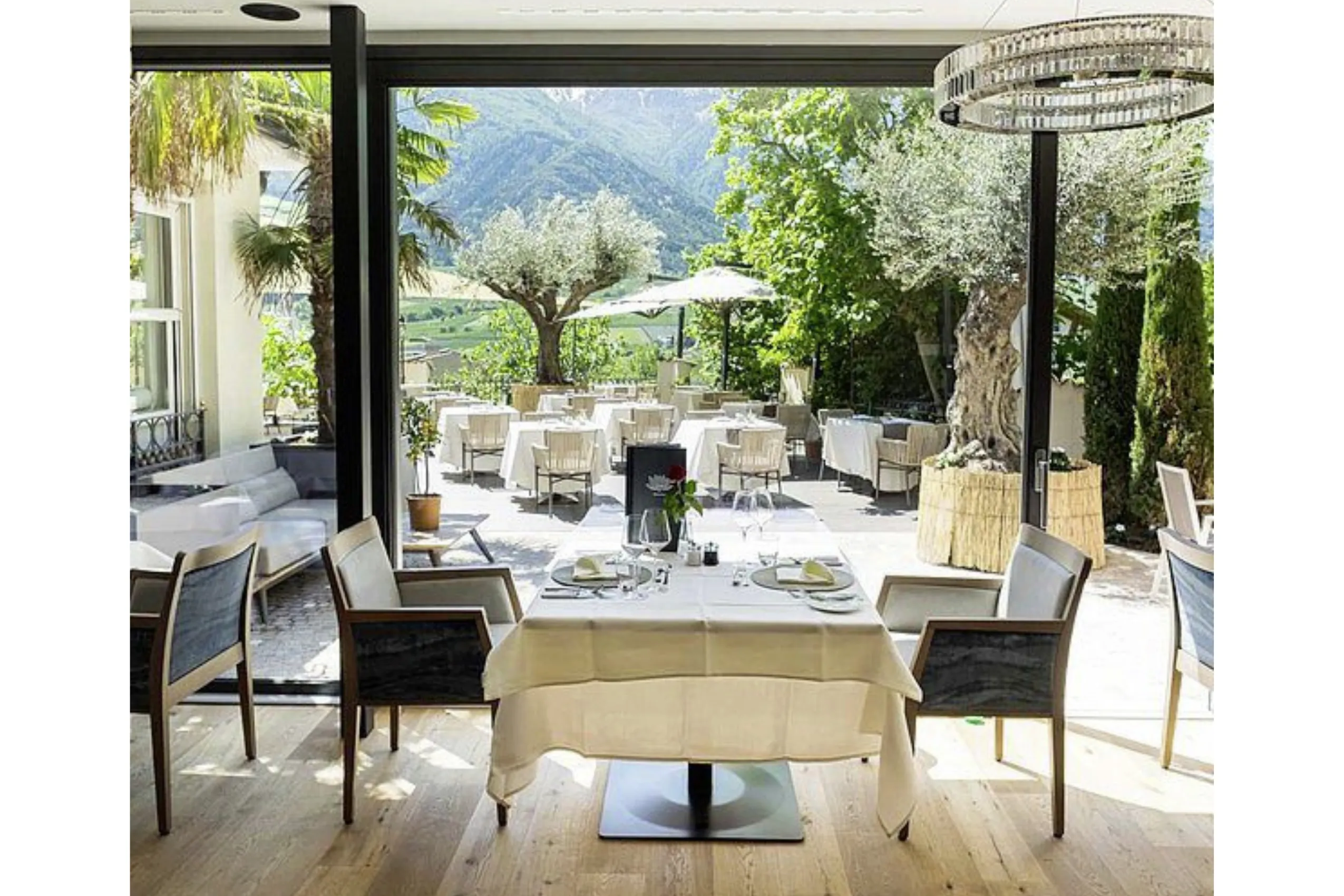DolceVita-Stube mit ge&ouml;ffnetem Fenster zu Terrasse mit Olivenb&auml;umen und Bergblick im Preidlhof Luxury DolceVita Resort