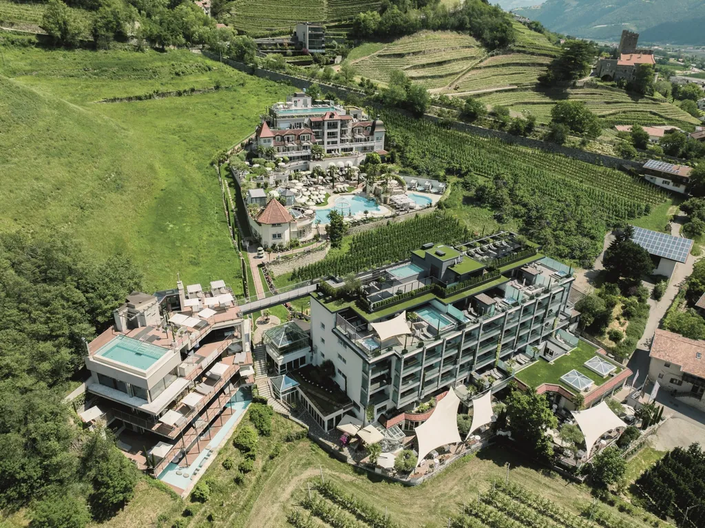 Vogelperspektive auf den Preidlhof Luxury DolceVita Resort mit den Gebäuden, schön angelegten Gärten und Pools.