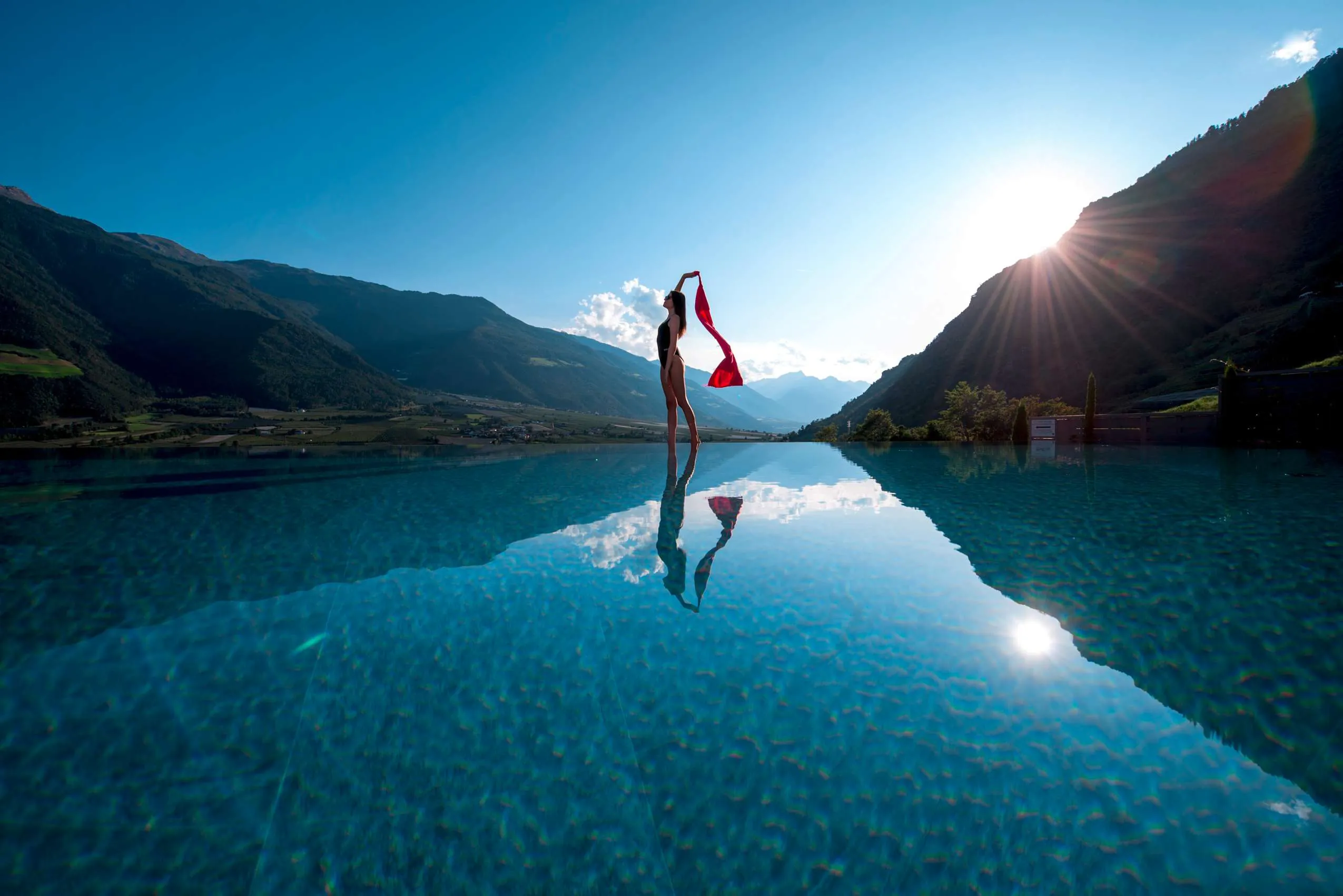 junge Frau steht am Beckenrand des Rooftop Infinity-Pools und hat ein rotes Tuch in der Hand, dass im Wind weht.