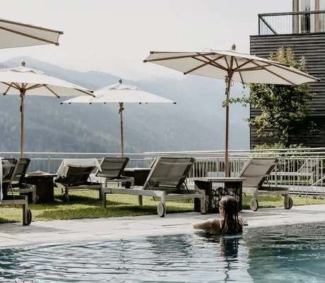 Frau mit Sonnenbrille schaut vom Outdoorpool des Das Kronthaler auf die Berge