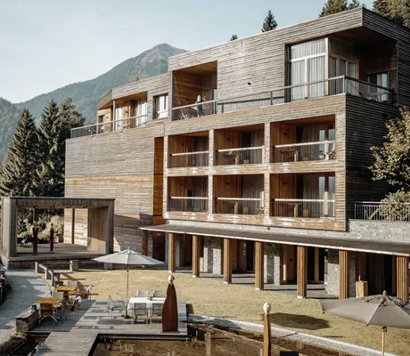 Holzfassade des Chaletgebäudes des Das Kronthaler mit weißen Sonnenschirmen davor
