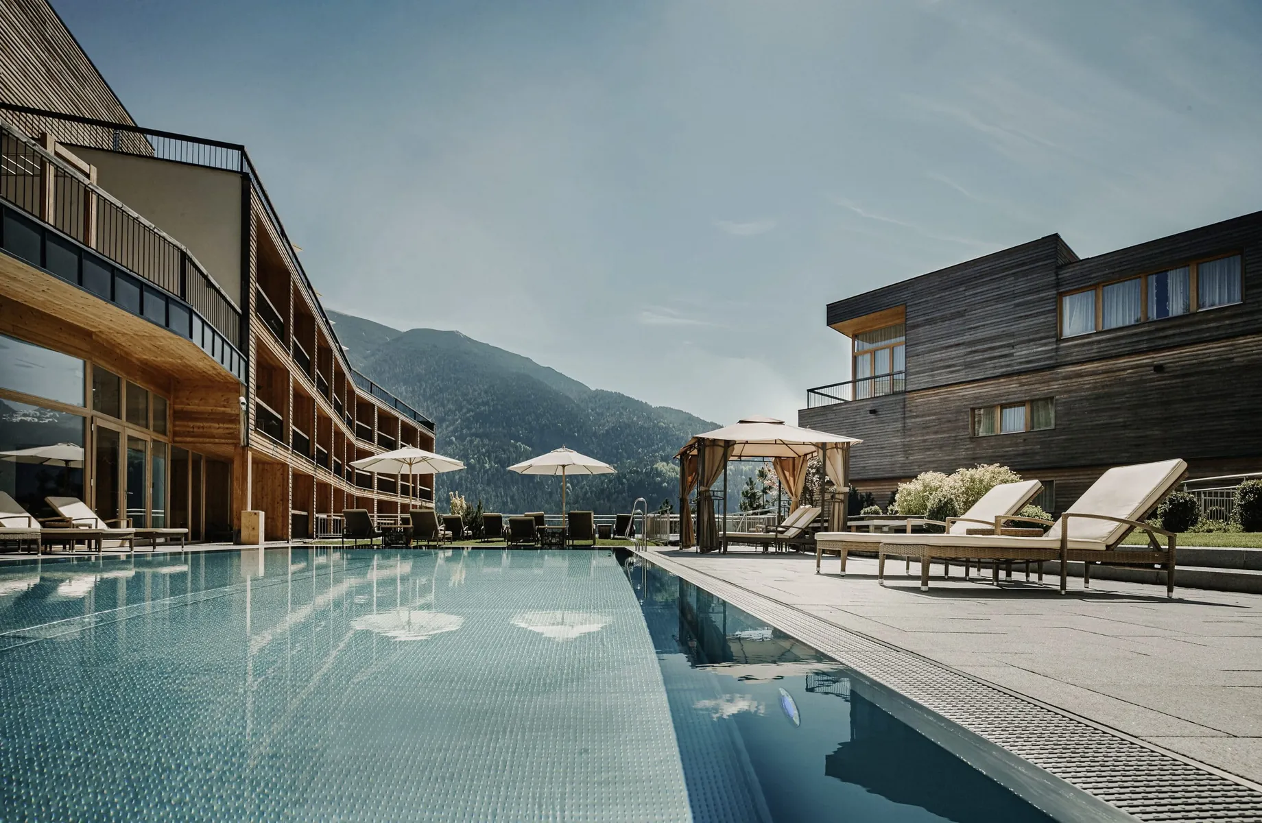 Outdoorpool des Das Kronthaler neben Fassade mit weißen Sonnenliegen am Rand