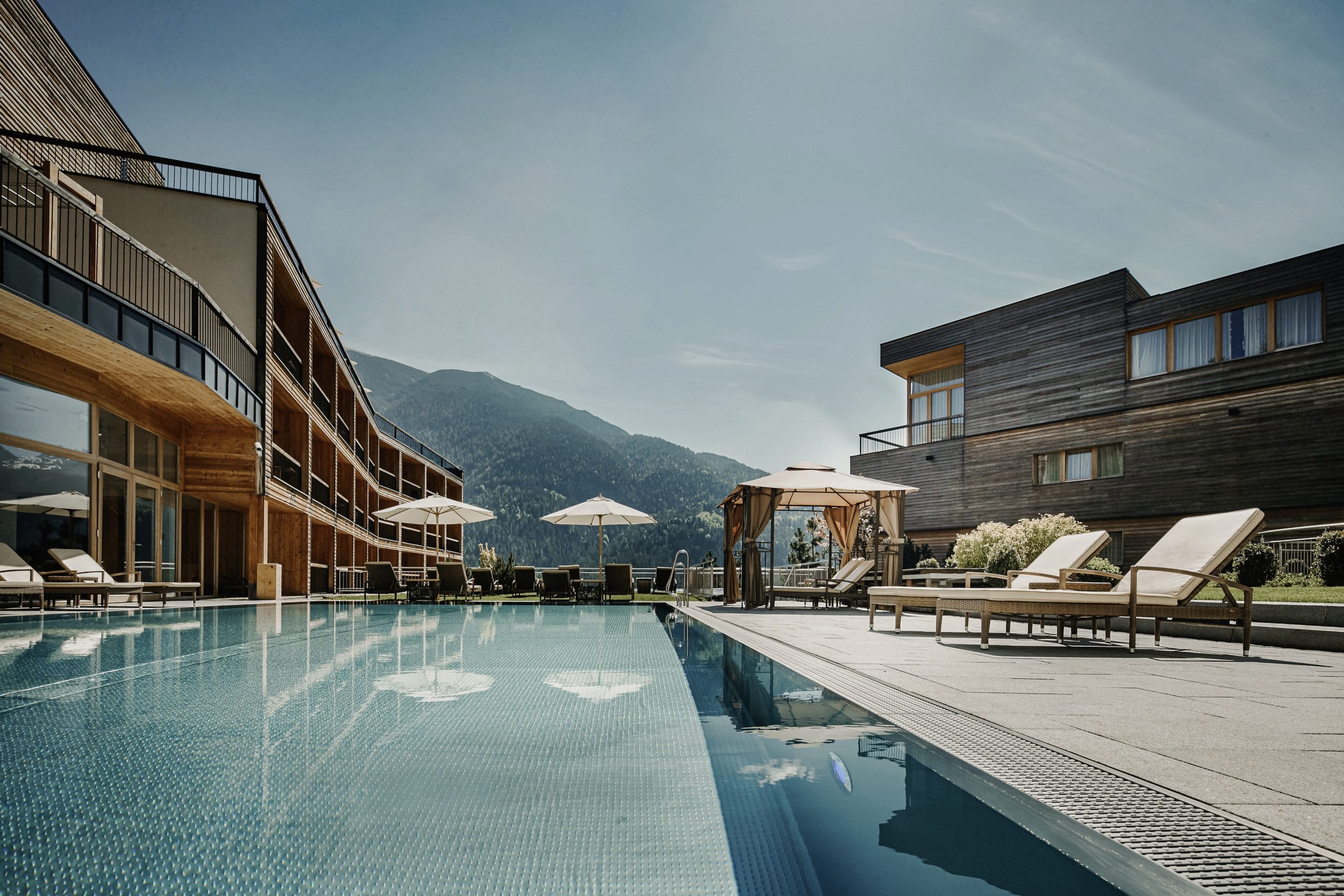 Outdoorpool des Das Kronthaler neben Fassade mit weißen Sonnenliegen am Rand
