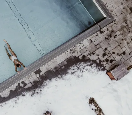 Frau in weißem Badeanzug im Outdoorpool des Das Kronthaler im Winter von oben