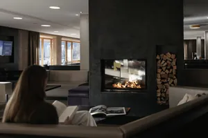 langhaarige Frau sitzt vor dem Kaminfeuer in der Lounge des Das Kronthaler und liest ein Buch
