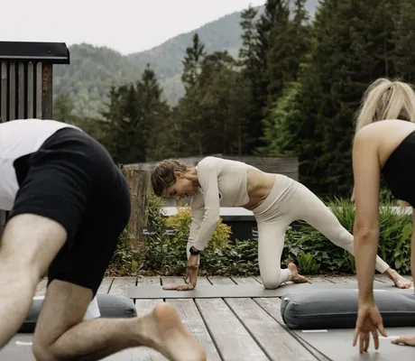 Yogagruppe praktiziert Yoga auf der Holzplattform vor dem angrenzenden Wald des Das Kronthaler