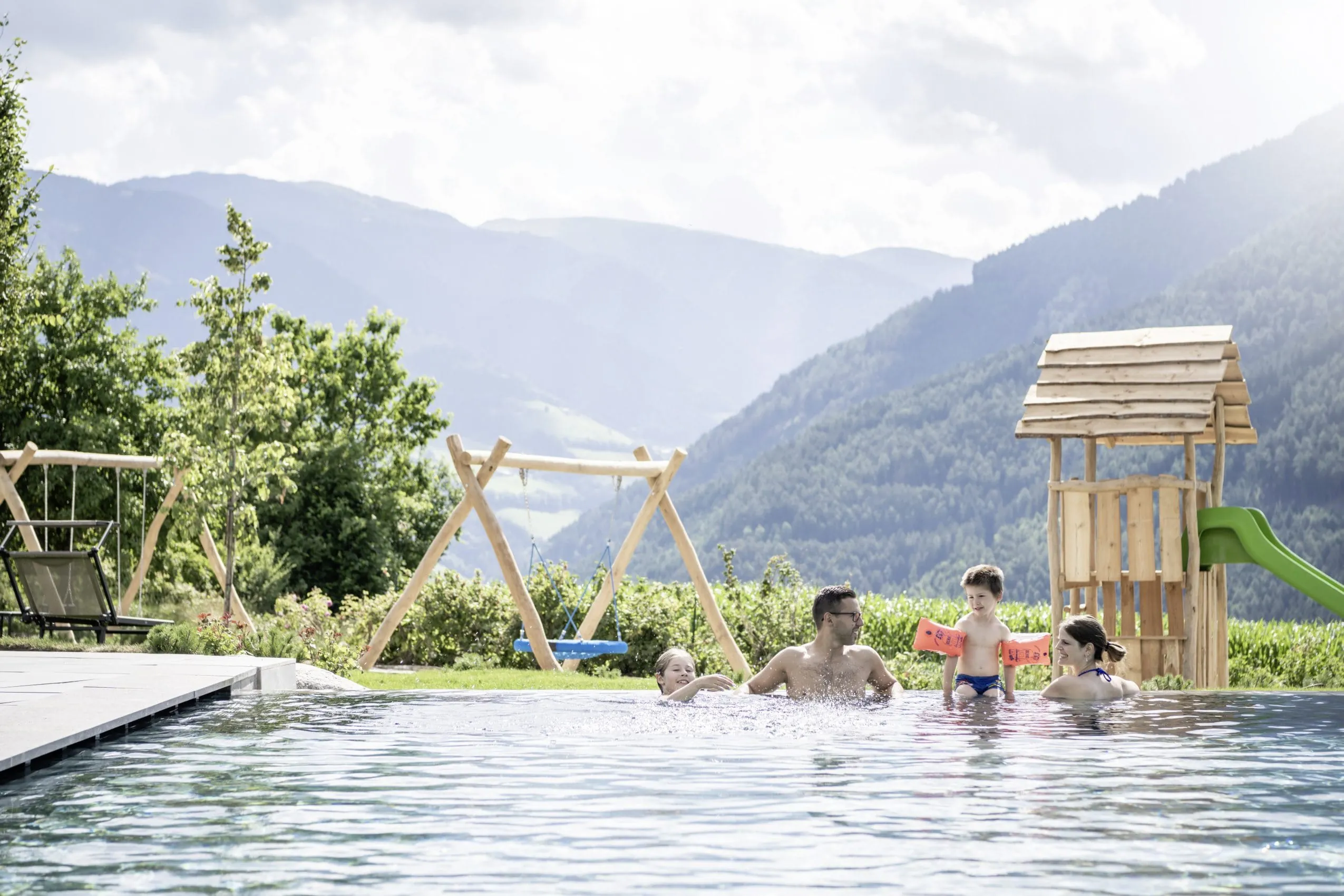 Eltern mit ihren beiden Kindern am Rand des Outdoorpools mit Blick auf die umgebenden Berge im Familienhotel Das Mühlwald