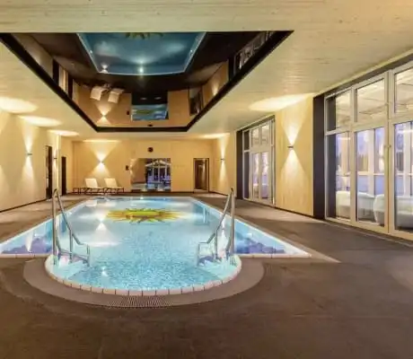 Indoorpool mit Sonnen-Mosaik am Boden des Schwimmbeckens, Echtholzwandverkleidung und edler Deckenverspiegelung.