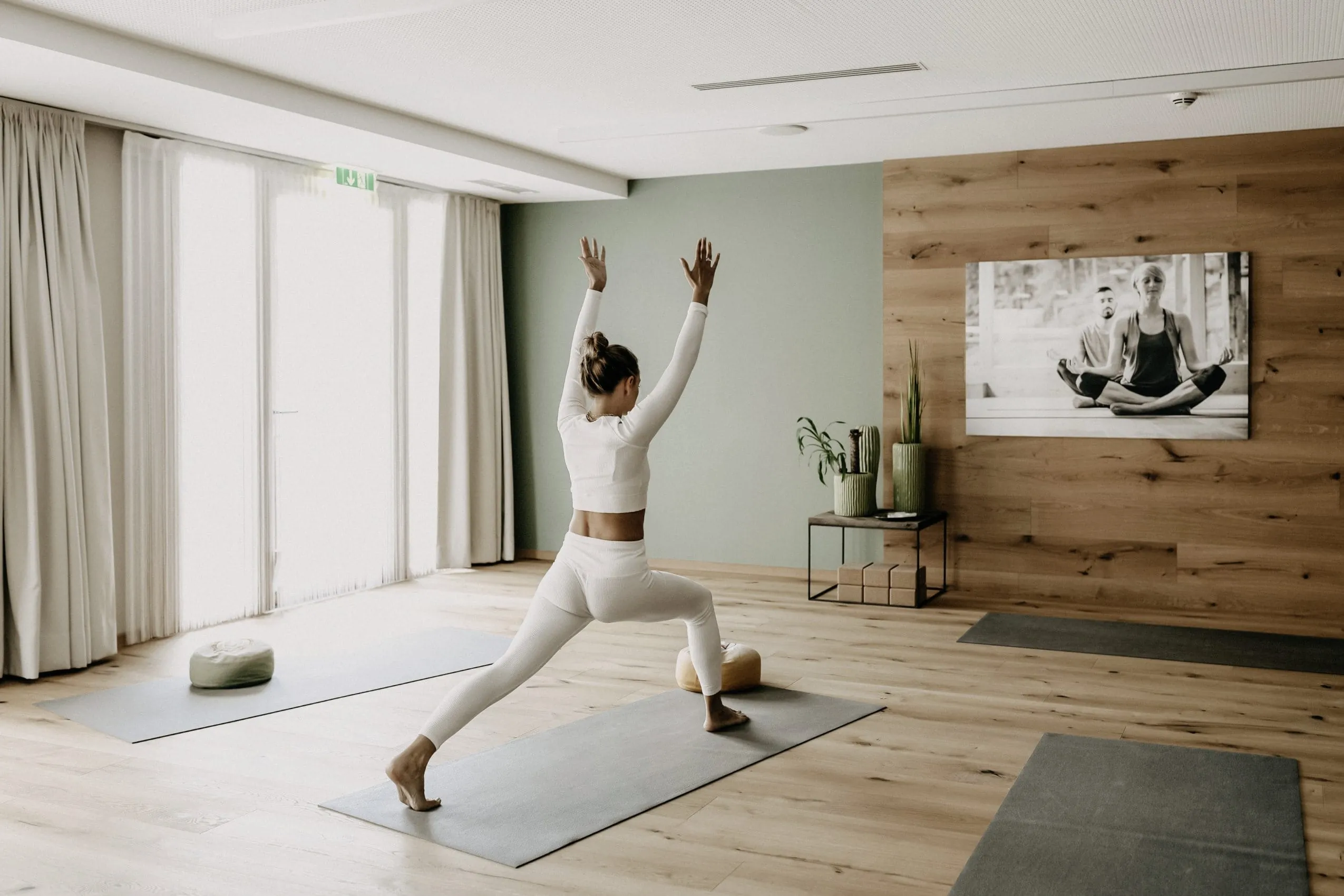 Junge Frau im Ausfallschritt und Armen Richtung Decke steht auf Matte im Yoga-Raum des Kronthaler