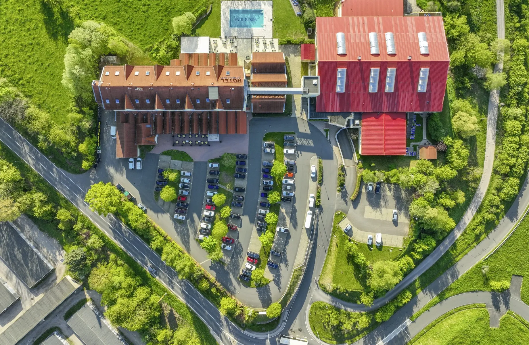 Aufnahme des Fair Resort von oben mit Hotelgebäude, Sport- und Wellnesskomplex, Outdoorpool hinter dem Haus umringt von ganz viel Grünfläche.