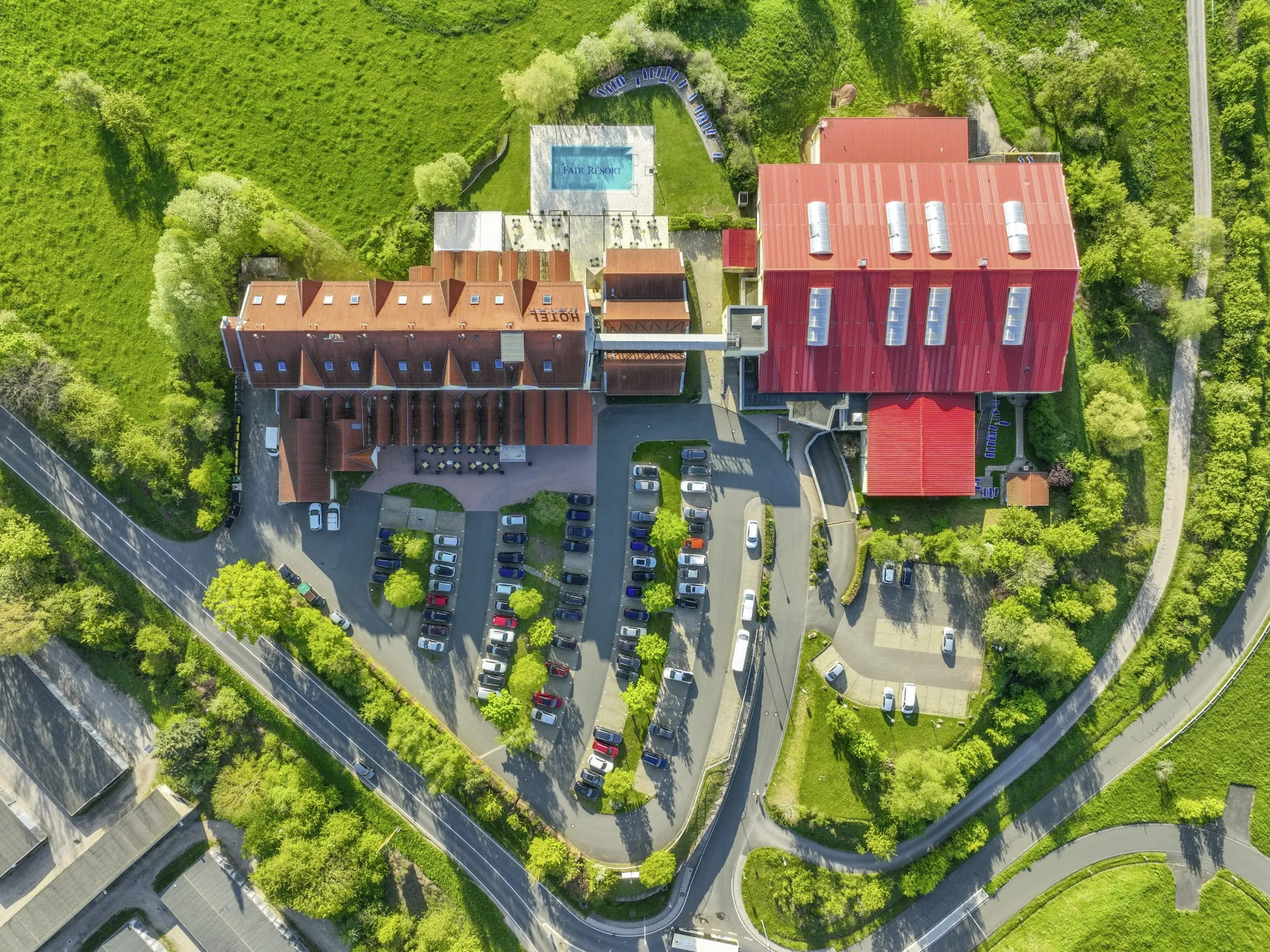 Aufnahme des Fair Resort von oben mit Hotelgebäude, Sport- und Wellnesskomplex, Outdoorpool hinter dem Haus umringt von ganz viel Grünfläche.