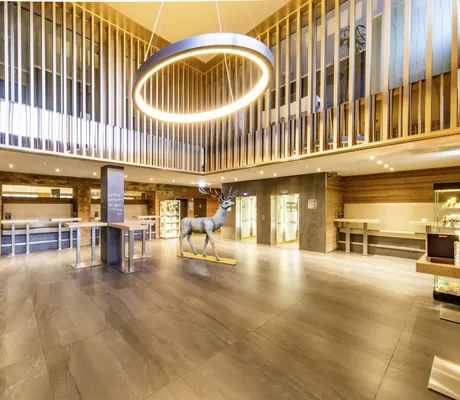 Eingangsbereich des Fair Resort mit Galerie, herabhängender Ringleuchte, schicker Hotelbar und riesiger Hirschfigur.