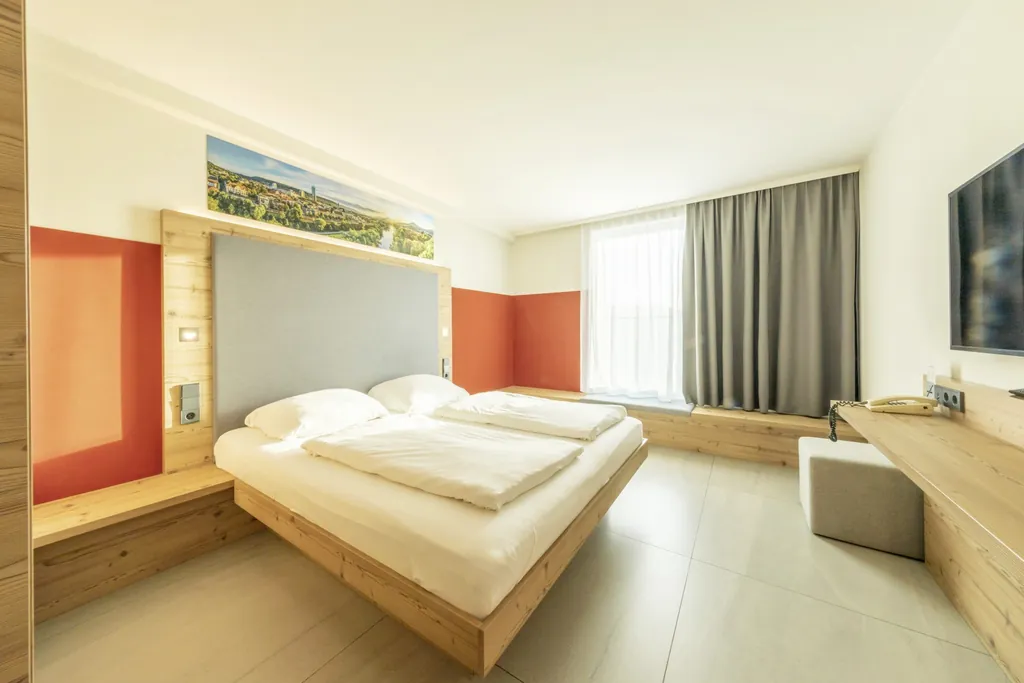 Zimmer des Wellnesshotels Fair Resort in Jena mit Doppelbett und heimischen Hölzern rund ums Bett sowie beim Schreibtisch.