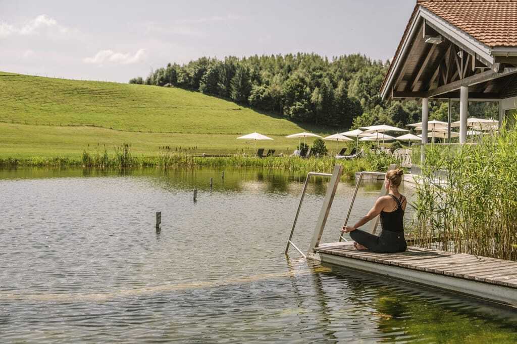 Frau meditiert auf dem Steg zum Natursee im Haubers Naturresort