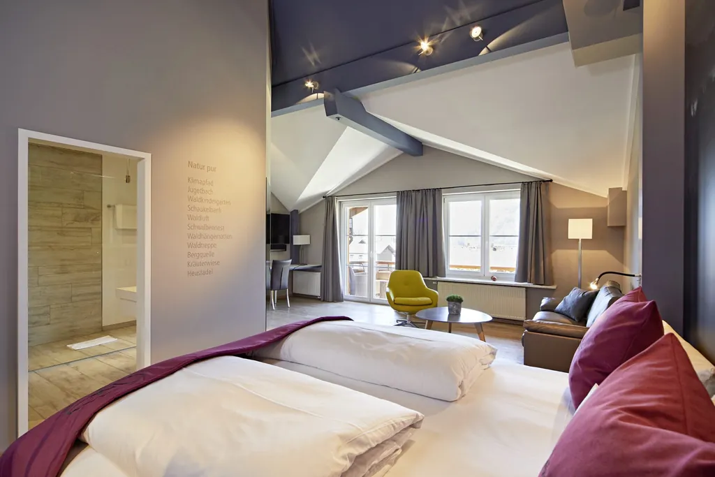 Doppelzimmer im Golfhotel Haubers Naturresort mit Balkon, Sofamöbeln und roten Farbakzenten