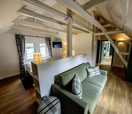 grünes Sofa im Wohnbereich unter weißen Balken im Hotel FreiWerk