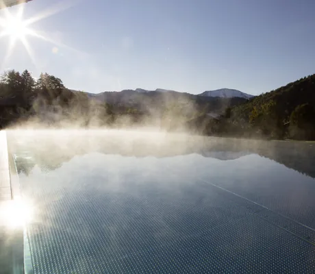 Outdoorpool im Morgendunst mit strahlendem Sonnenschein in Haubers Naturresort