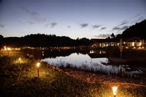 illuminierter Natursee mit Haus am See am Abend in Haubers Naturresort