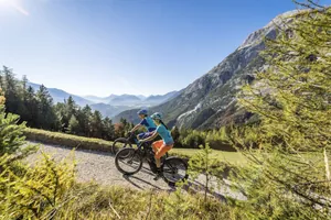 Zwei Personen in Sportkleidung auf einem E-Bike umgeben von grüner Natur und Blick auf den Berg Hohe Munde in der Nähe des Alpin Resort Sacher Seefeld