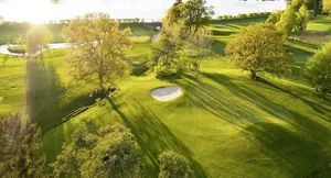 Blick von oben auf den grünen, mit Bäumen bepflanzten Golfplatz Rieden direkt am Wertach-Stausee