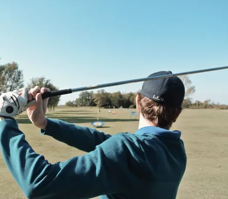 Blick auf einen Golfspieler von hinten mit geschwungenem Golfschläger in der Hand auf dem Golfplatz des Tenuta Primero Grado Family Collection