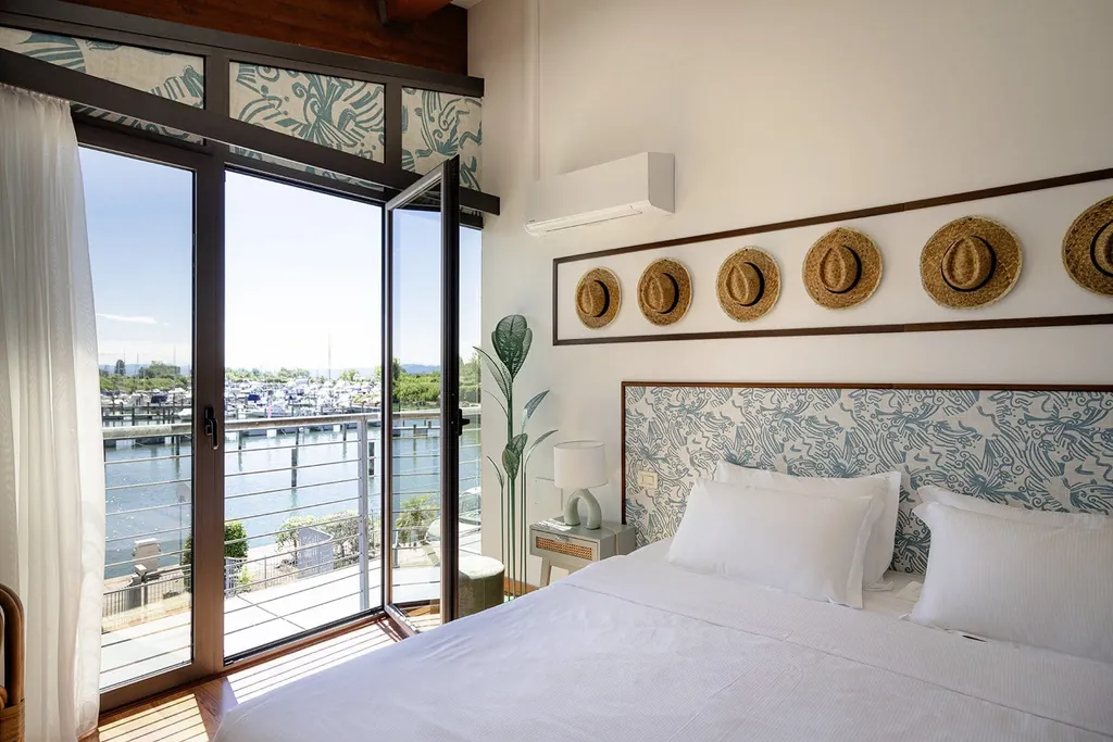 Schlafzimmer einer Unterkunft des Tenuta Primero Grado Family Collection mit Doppelbett, mehreren dekorativen Strohhüten an der Wand und Blick auf den Yachthafen