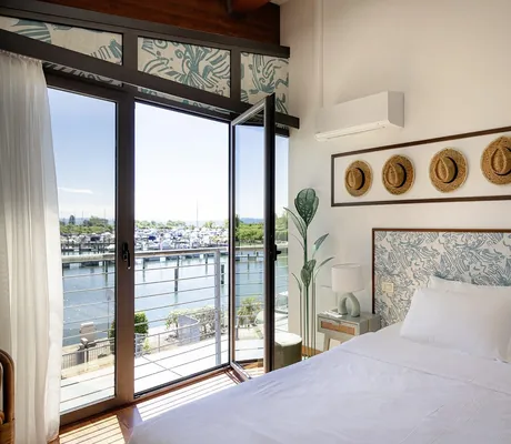 Schlafzimmer einer Unterkunft des Tenuta Primero Grado Family Collection mit Doppelbett, mehreren dekorativen Strohhüten an der Wand und Blick auf den Yachthafen