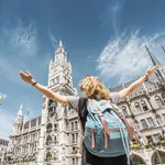 Junge Frau mit Rucksack steckt auf dem Marienplatz in München und blickt Richtung Glockenturm