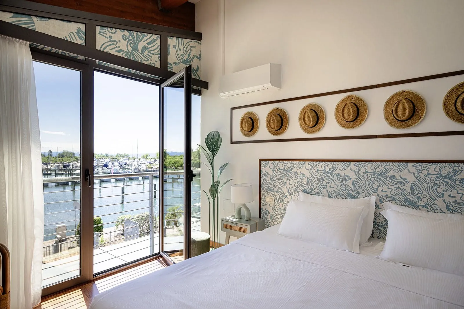 Schlafzimmer einer Unterkunft des Tenuta Primero Grado Family Collection mit Doppelbett, mehreren dekorativen Strohh&uuml;ten an der Wand und Blick auf den Yachthafen